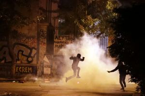 A protester jumps to avoid tear gas as another one prepares to throw a firebomb during a protest against the visit of US ...