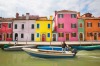 Burano island's colourful houses on canal where man is leaving in small fish boat.