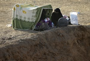 In this Thursday, Nov. 17, 2016 photo, Iraqi women, who fled the fighting between Iraqi forces and Islamic State militants, sit at an open field as they wait to cross to the Kurdish controlled area, in the Nineveh plain, northeast of Mosul, Iraq.