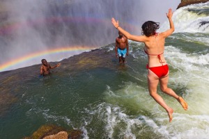 Woman jumps into Devil's Pool at Victoria Falls. It looks like she will be swept over the waterfall but a thick lip of ...