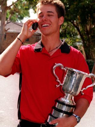 Golfer Aaron Baddeley holding Australian Open trophy and talking on mobile phone outside Channel 9 studios 29 Nov 1999.