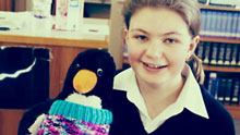 picture of Adelaide holding a stuffed toy penguin wearing one of the jumpers she knitted.