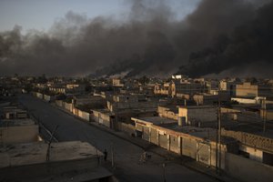 A man rides his bike on a street as smoke rises from burning oil fields in Qayara, some 50 kilometers south of Mosul, Iraq, Monday, Oct. 31, 2016.