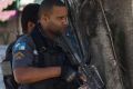 Police on an anti-drug trafficking operation patrol as a woman pushes a child along the sidewalk in the Cidade de Deus ...