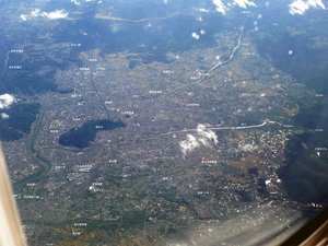 An aerial photo of a portion of Fukushima Basin, facing south. The Ōu Mountains can be seen along the right side of the image. Mt. Shinobu can be seen in the center-left as the mountain surrounded by the city, with the Abukuma River flowing south-north to the east (left) of Mt. Shinobu.