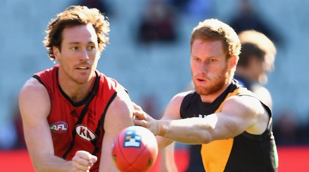 Mitch Brown of the Bombers handballs while being tackled by Tiger Nick Vlaustin.