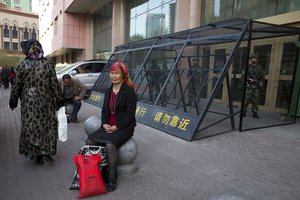 FILE - In this May 1, 2014 file photo, a Uighur woman rests near a cage protecting heavily armed Chinese paramilitary policemen on duty in Urumqi in China's northwestern region of Xinjiang.