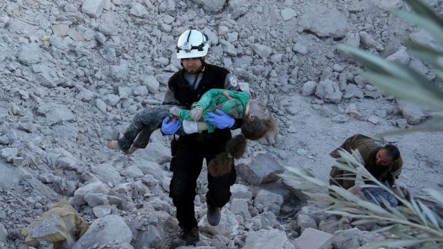 A man carries a wounded child over the wreckage of collapsed buildings after Russian forces carried out air strikes on ...