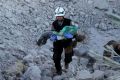 A man carries a wounded child over the wreckage of collapsed buildings after Russian forces carried out air strikes on ...