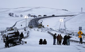 Demonstrators sit on a closed bridge across from police protecting the Dakota Access oil pipeline site next to the Oceti Sakowin camp where people have gathered to protest the pipeline near Cannon Ball, N.D., Wednesday, Nov. 30, 2016.