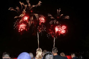 Red and gold fireworks light up the sky as people watch on.