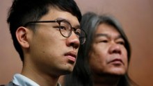 Headshots of Nathan Law and Leung Kwok-hung side-by-side watching a news conference.