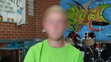 A young boy wearing a green shirt in a music room at a detention centre.