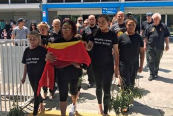 Aboriginals file out of  Launceston airport with remains in box under flag.