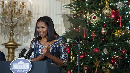 First Lady Michelle Obama speaking at a podium in front of a Christmas tree.