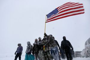 Military veterans huddle together to hold a United States flag against strong winds during a march to a closed bridge ...