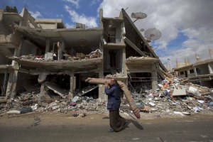 File - In this April 14, 2016 photo, a Syrian man carries a carpet through a devastated part of the town of Palmyra as families load their belongings onto buses in the central Homs province in Syria.