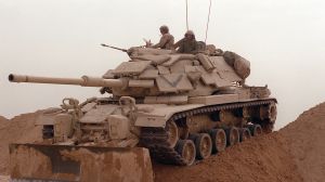 A tank negotiates a sand berm during an operation in the Gulf War.