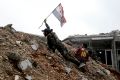 A Syrian army soldier places a Syrian national flag during a battle with rebel fighters at the Ramouseh front line, east ...