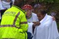 An ambulance officer comforts cyclists after a woman was killed on Mona Vale Road, Pymble.