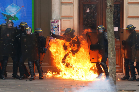 A French riot police officer gesturea as he is surrounded by flames, during a demonstration against the controversial labour reforms of the French government in Paris on September 15, 2016. Opponents of France's controversial labour reforms took to the streets on September 15, 2016 for the 14th time in six months in a last-ditch bid to quash the measures that lost the Socialist government crucial support on the left. Scores of flights in and out of France were cancelled as air traffic controllers went on strike to try to force the government to repeal the changes that became law in July. / AFP PHOTO / Thomas SAMSONTHOMAS SAMSON/AFP/Getty Images