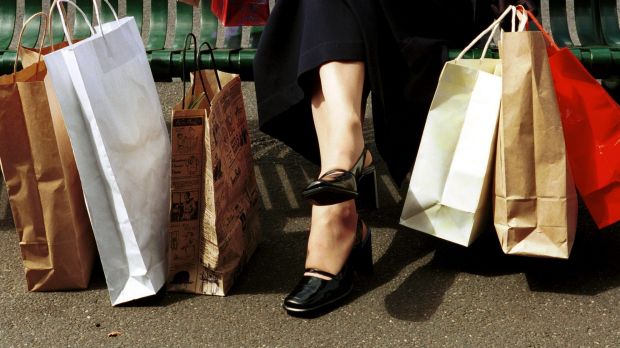 RETAIL . Generic . Woman in a long skirt sitting at a bus stop with her shopping in paper bags as Autumn leaves pass her ...