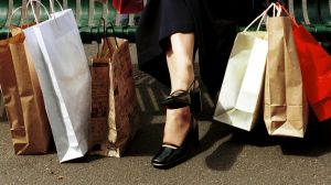 RETAIL . Generic . Woman in a long skirt sitting at a bus stop with her shopping in paper bags as Autumn leaves pass her ...