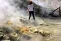 A woman takes a close look at a steaming fumarola at the Solfatara crater bed in the Campi Flegrei near Naples, Italy. 