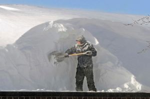 Cody Rohrich chips away at a large snowdrift while working in the blowing snow on a rooftop in downtown Bismarck on ...