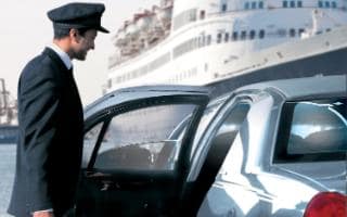 A chauffeur opening the door of a car with a cruise ship in the background