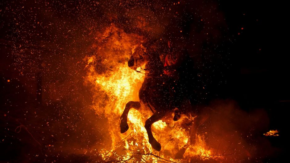 A A woman rides a horse through a bonfire during 'Las Luminarias' Festival.