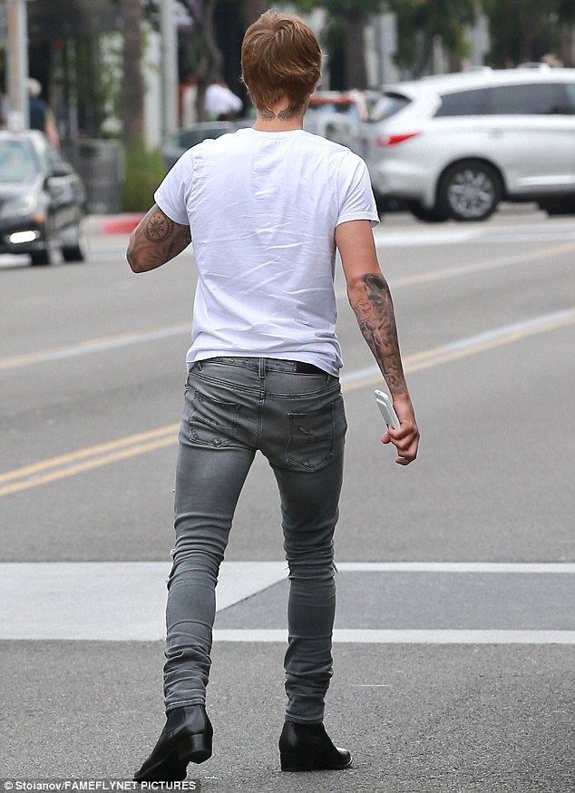 Finishing touches: The 22-year old teamed his spray on denim with a simple white T-shirt that fully exposed his intricate sleeve tattoos