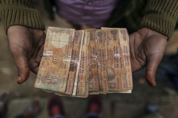 A weaver displays ten rupees Indian banknotes for a photograph in Varanasi, Uttar Pradesh, India