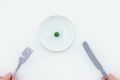 Woman holding miniature knife and fork by plate with single pea tiny plates. Serving size.