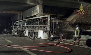 A firefighter sprays water on the burned hulk of a bus that crashed and burst into flames near Verona, northern Italy, Saturday, Jan. 21, 2017.