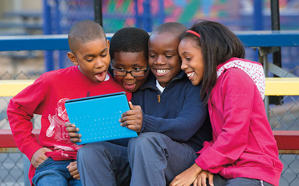 image of four children sitting on a bench sharing a surface tablet