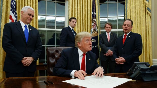 Vice President Mike Pence watches at left as President Donald Trump prepares to sign his first executive order in the ...