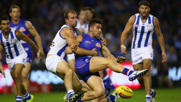 Marcus Adams of the Bulldogs tries to get a kick away as he is tackled by Ben Cunnington of the Kangaroos.