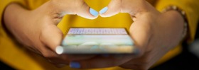 Young woman using cell phone to send text message on social network at night. Closeup of hands with computer laptop in ...