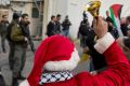 Palestinian protesters, some are dressed as Santa Claus, carry Palestinian flags and chant anti-Israel slogans in front ...