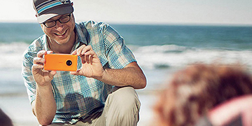 Man taking a photo of his family on a beach with an orange Lumia 830 phone 
