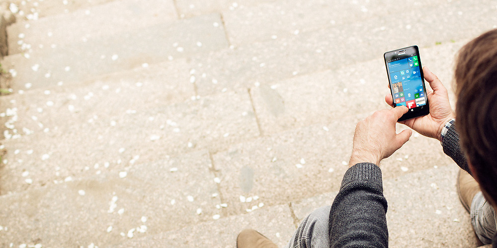 Man sitting on steps outside, looking at the start screen of his Lumia phone 
