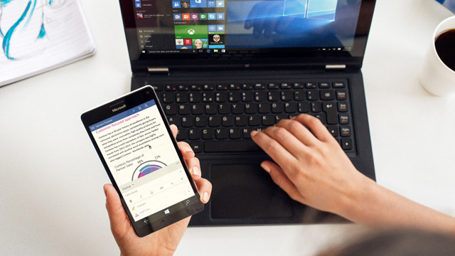 Woman's hands hovering over open laptop with Lumia 950 in the left hand