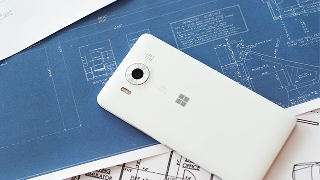 A white Lumia 950 display side down on top of blueprints on desk