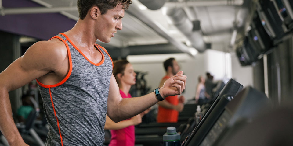 A man looks at Microsoft Band in his wrist while working out in a gym.