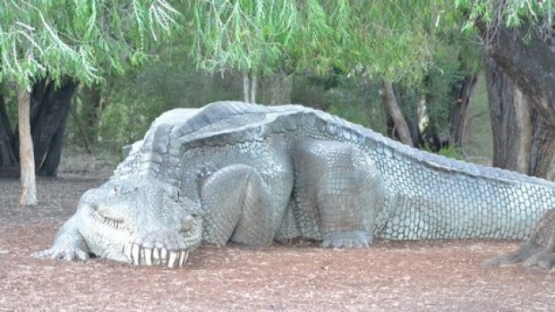 The child was playing on a crocodile statue when the man approached and picked up the child.