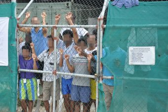 Asylum seekers stare at media from behind a fence