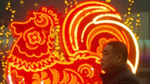 Chinese men walk past neon decorations marking the Year of the Rooster in Beijing, China, Monday, Jan. 16, 2017. The ...