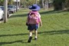 A child walks along grass towards school wearing a large pink backpack