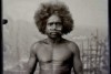 An Aboriginal man sits on a stool in a photography studio